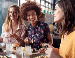a group of women talking and eating food in a restaurant