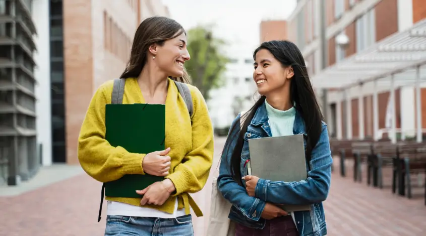 two young women walking outside and holding notebooks
